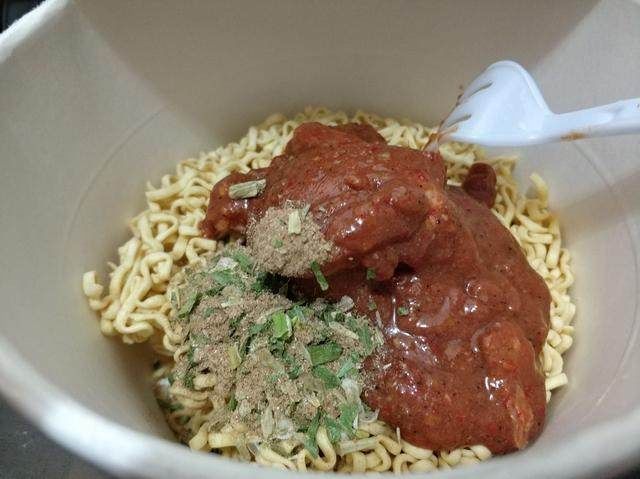 把调料包和肉包撕开后,挤到泡面上面,看 ,肉块被牛肉酱覆盖住了,牛肉