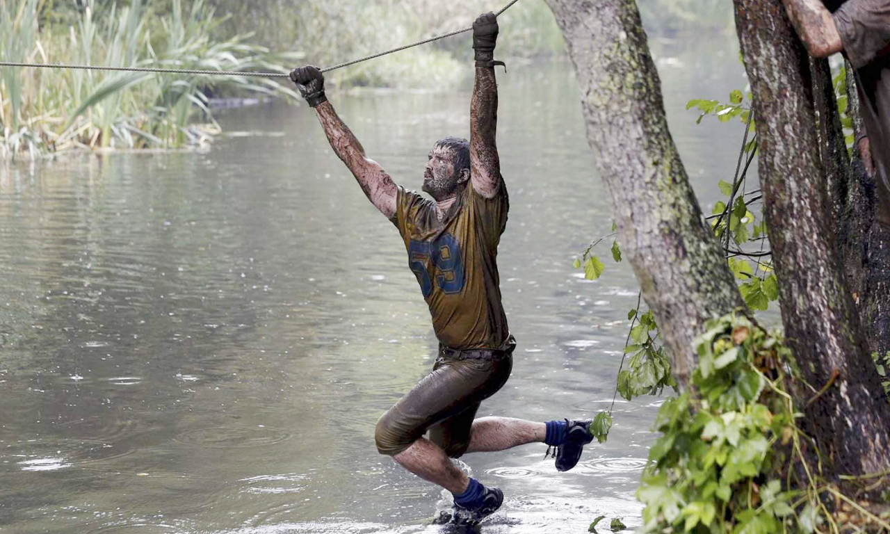 比赛中的障碍包括一座高墙，50英尺长的泥浆坑，拦货网，平衡木，并且要以团队的形态征服终点线前那个“声名狼藉”的泥坑。图为选手通过铁丝“桥”。