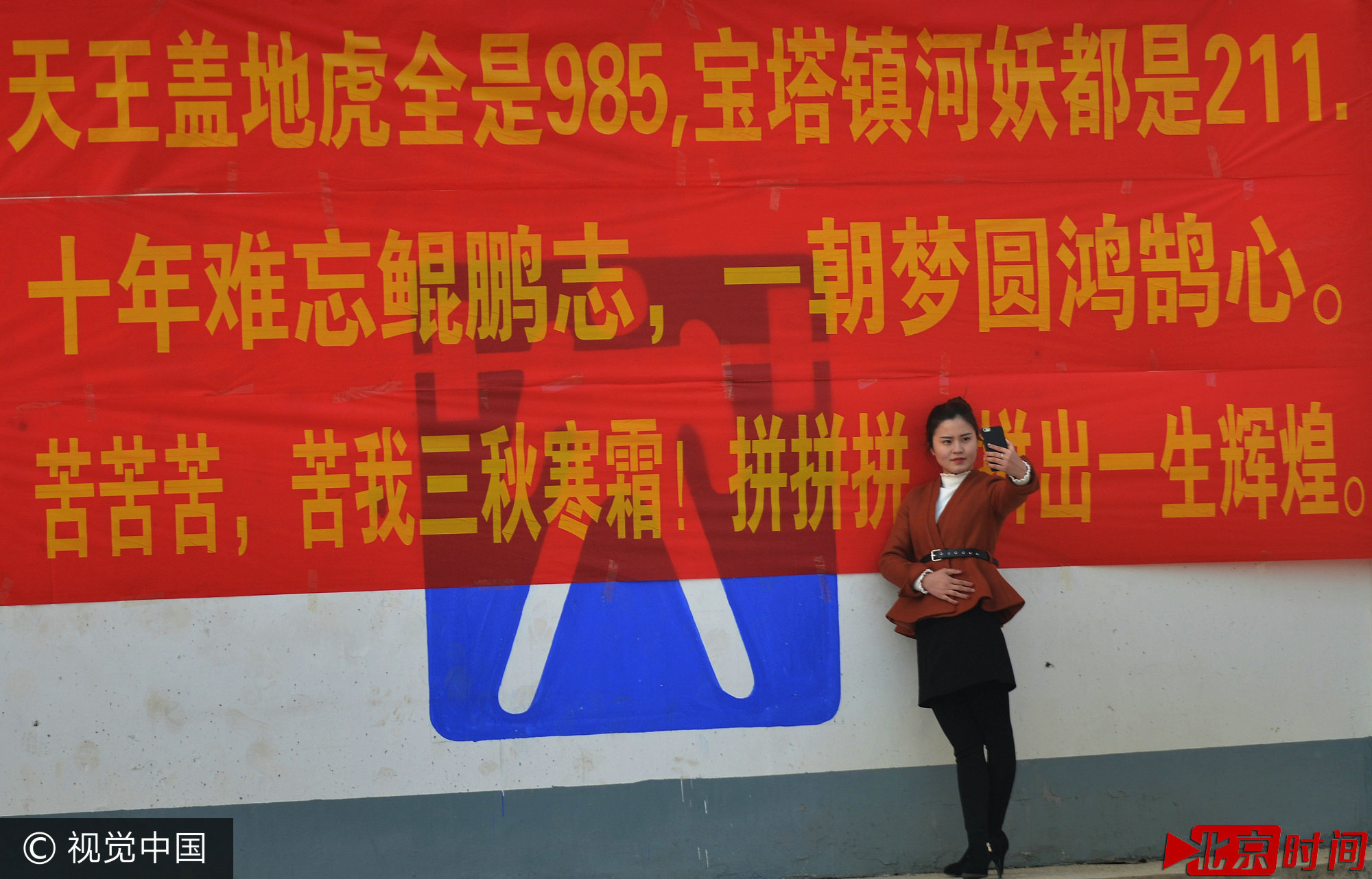 2017年2月19日，一名老师在河南夏邑县第一高级中学院内的励志标语前拍照。