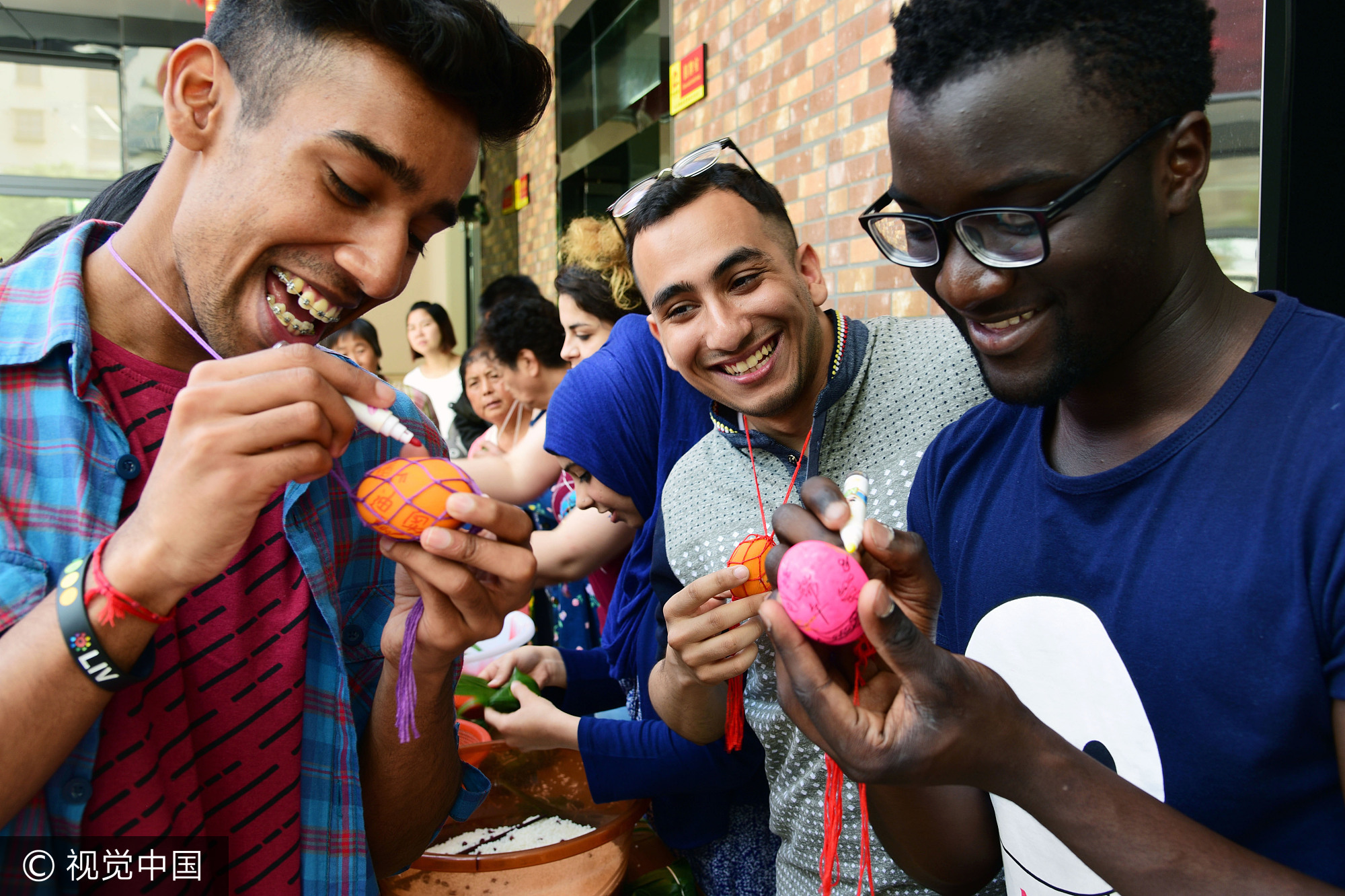 2017年5月25日，江苏镇江，社区居民在指导外国留学生包粽子。当日，端午节临近，江苏大学十多名来自赞比亚、印度、土耳其、巴基斯坦、南非等国的留学生走进镇江市和平路街道金江社区，在居民指导下学习包粽子、缝香囊，在咸鸭蛋上描画端午民俗，体验中国传统的端午文化。