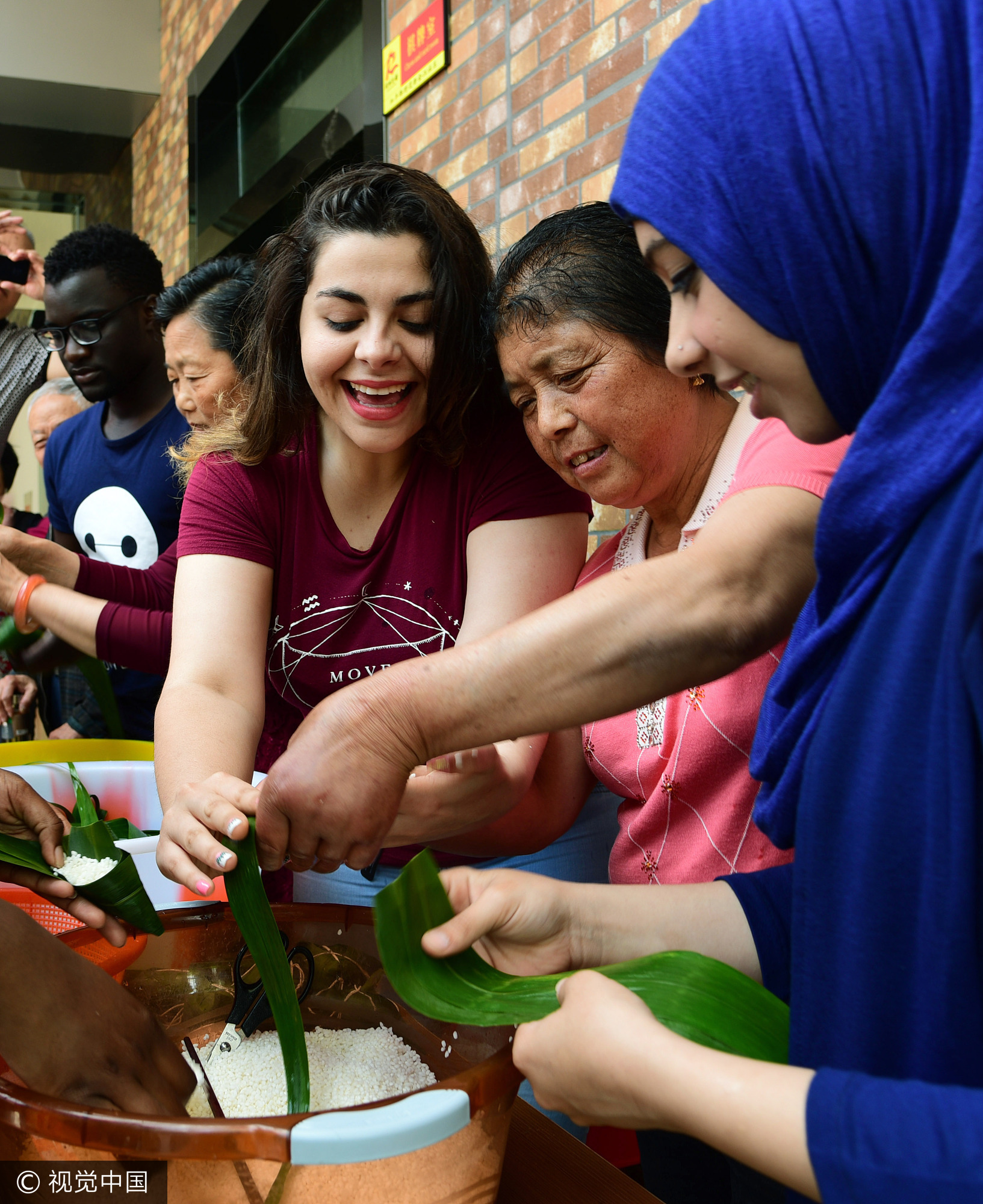 2017年5月25日,江苏镇江,社区居民在指导外国留学生包粽子。当日,端午节临近,江苏大学十多名来自赞比亚、印度、土耳其、巴基斯坦、南非等国的留学生走进镇江市和平路街道金江社区,在居民指导下学习包粽子、缝香囊,在咸鸭蛋上描画端午民俗,体验中国传统的端午文化。