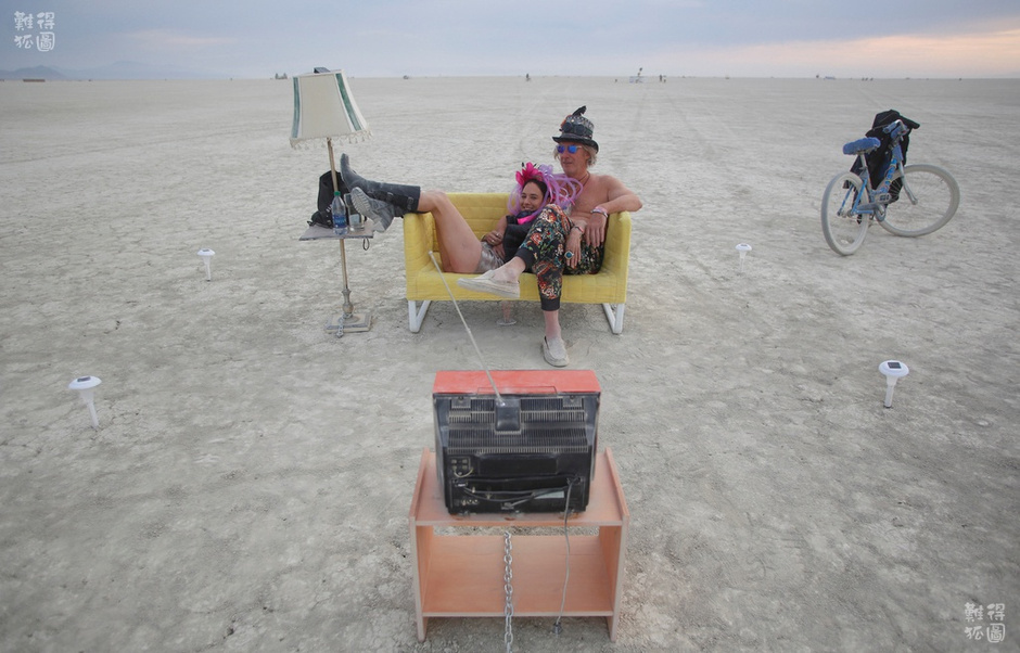 这样激发人们想象力和创造力的狂欢，吸引了全世界嬉皮士、雅皮士、少数派艺术人士以及科技巨头们。亚马逊的CEO贝索斯，以及FACEBOOK的创始人扎克伯格都是火人节的狂饭。特斯拉汽车的创始人伊隆·马斯科也曾经说过，“如果你想了解硅谷的精髓，就去火人节。”图为荒漠中的露天小客厅，一对情侣坐在沙发上看电视。