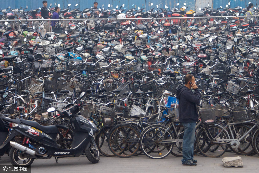 2010年10月9日，北京中关村海龙大厦外自行车停车场，一名市民正在拨打电话。他身后自行车、电动车、摩托车紧密摆放。